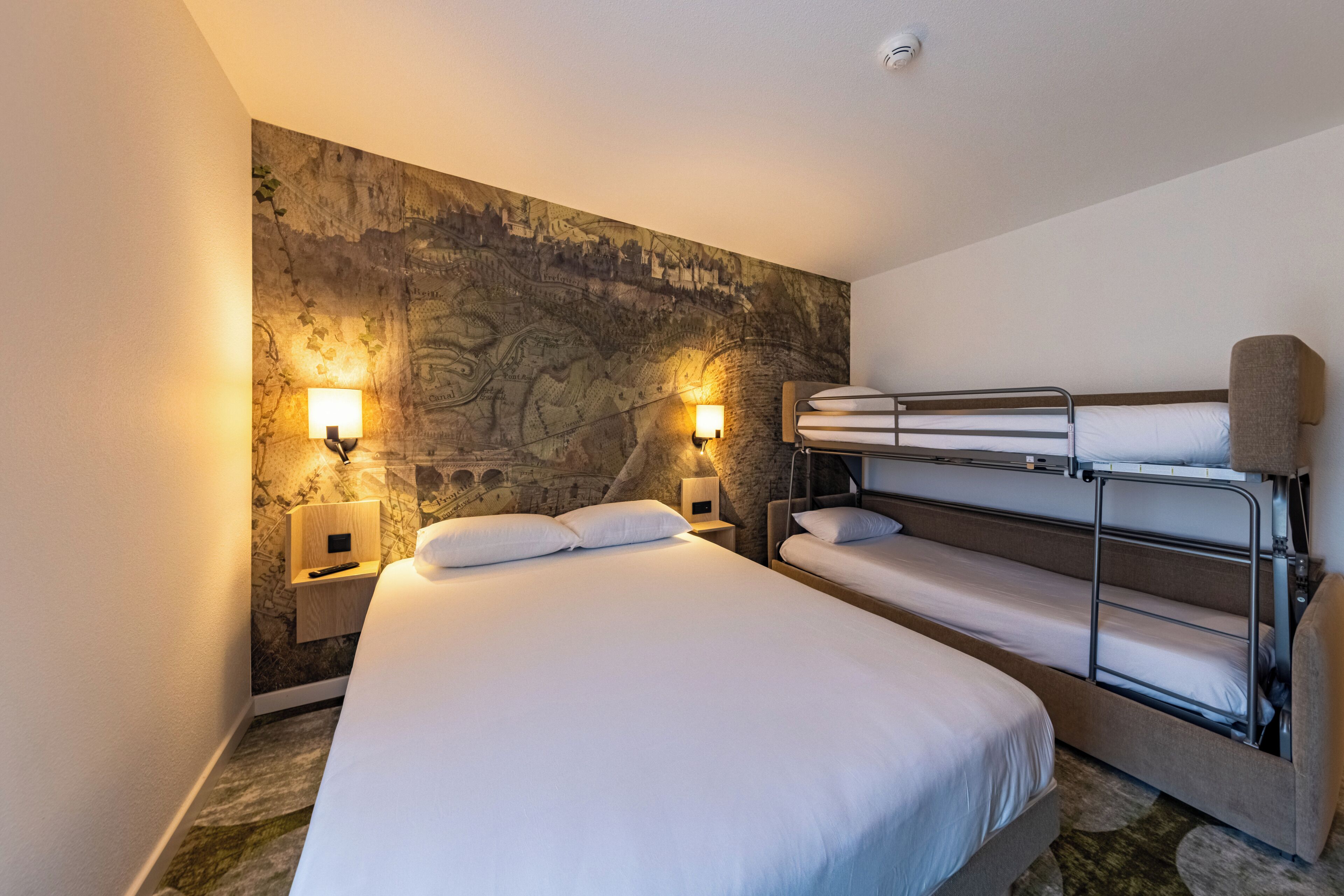 Une chambre d’hôtel avec un grand lit, un lit superposé et deux lampes fixées au mur.