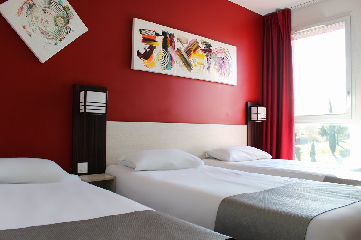 Une chambre d’hôtel avec deux lits, un mur rouge et un grand tableau abstrait.