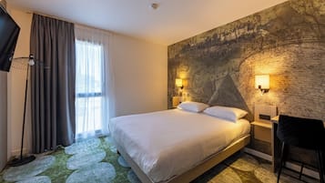 Habitación de hotel con una cama grande, un escritorio con silla, un televisor y una ventana con cortinas.