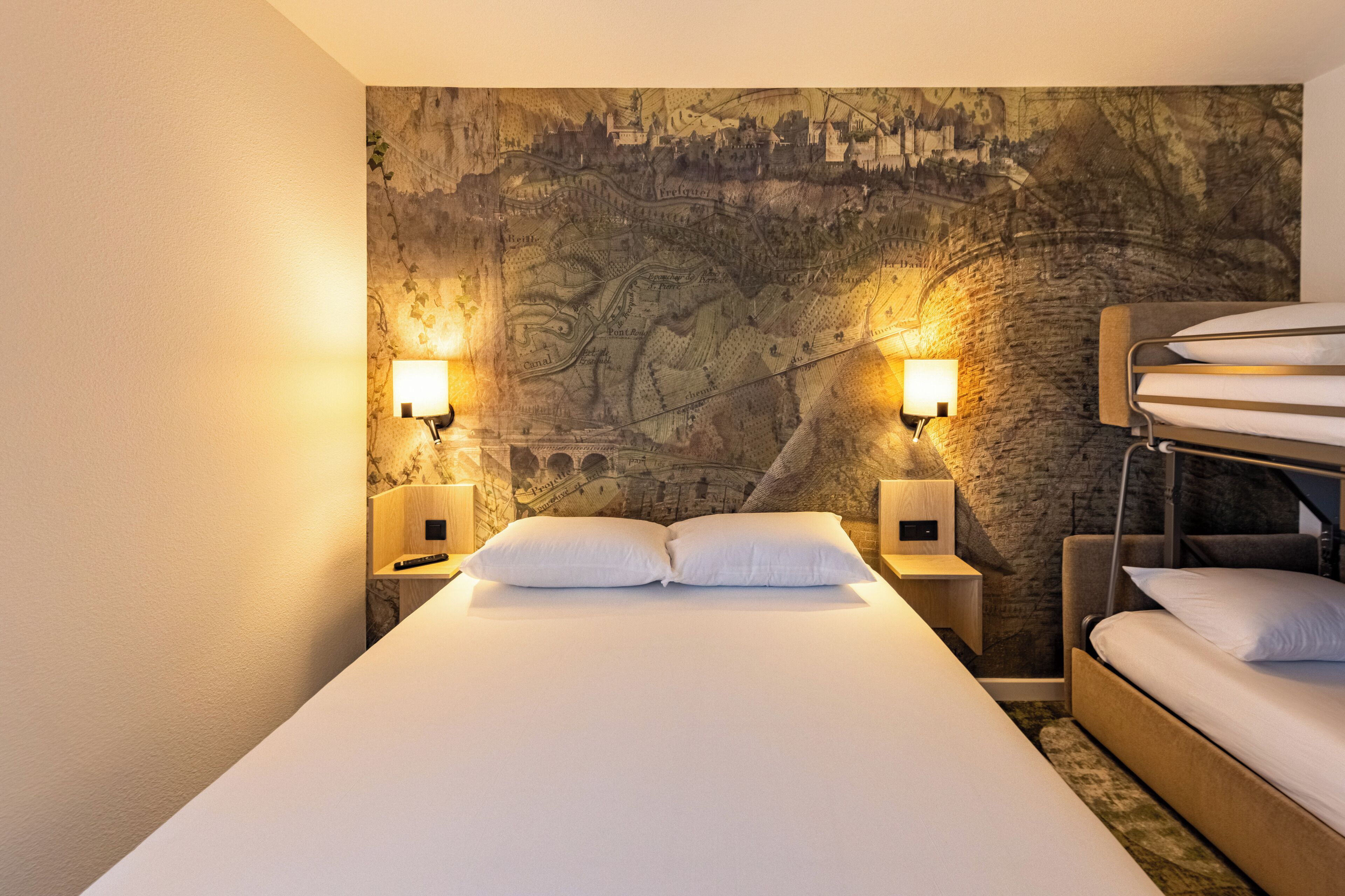 Una habitación de hotel con una cama grande, dos mesitas de noche, un mapa colgado en la pared y una litera.