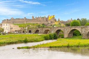 Un puente de piedra histórico con varios arcos sobre un río, que conduce a un castillo fortificado con torres y un foso.