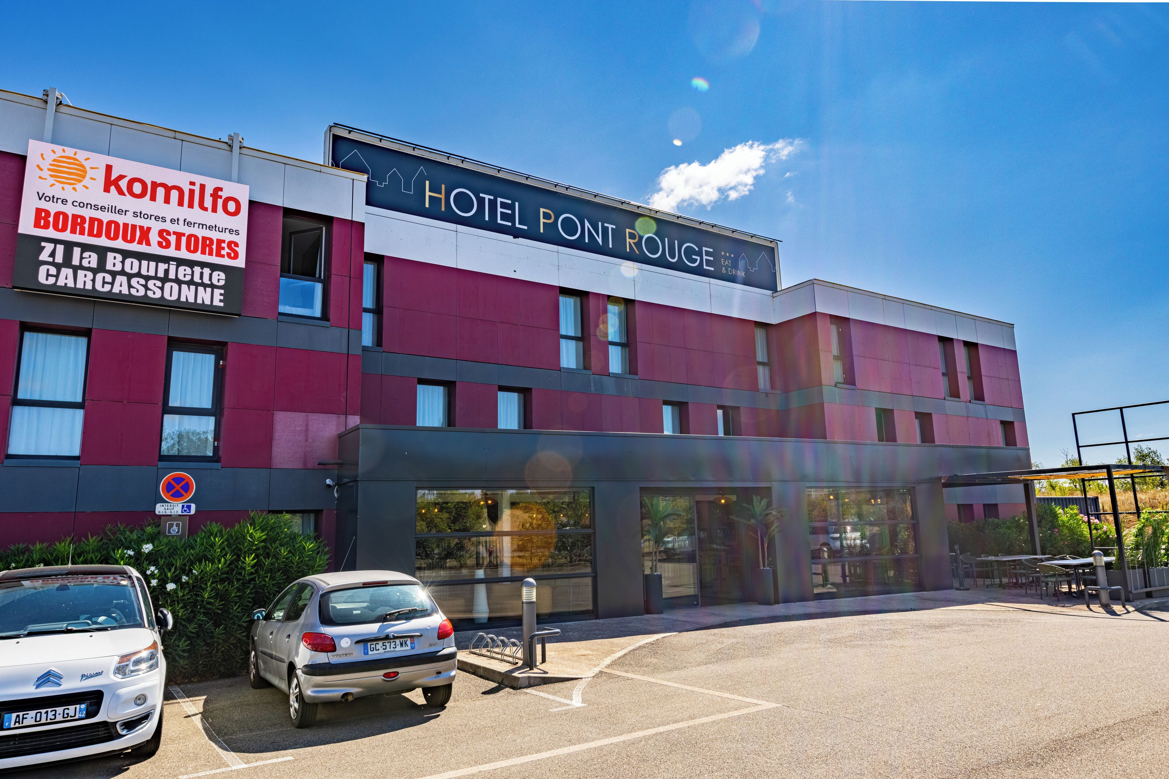 Un hotel llamado "HOTEL PONT ROUGE" con un cartel que indica "komilfo BORDOUX STORES" y "ZI la Bouriette CARCASSONNE" en la fachada.
