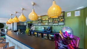 A bar area with a long counter, hanging wicker pendant lights, shelves with liquor bottles, and a pink bucket labeled "Premiere Bulle". - Hôtel Pont Rouge, Carcassonne (Carcassonne)