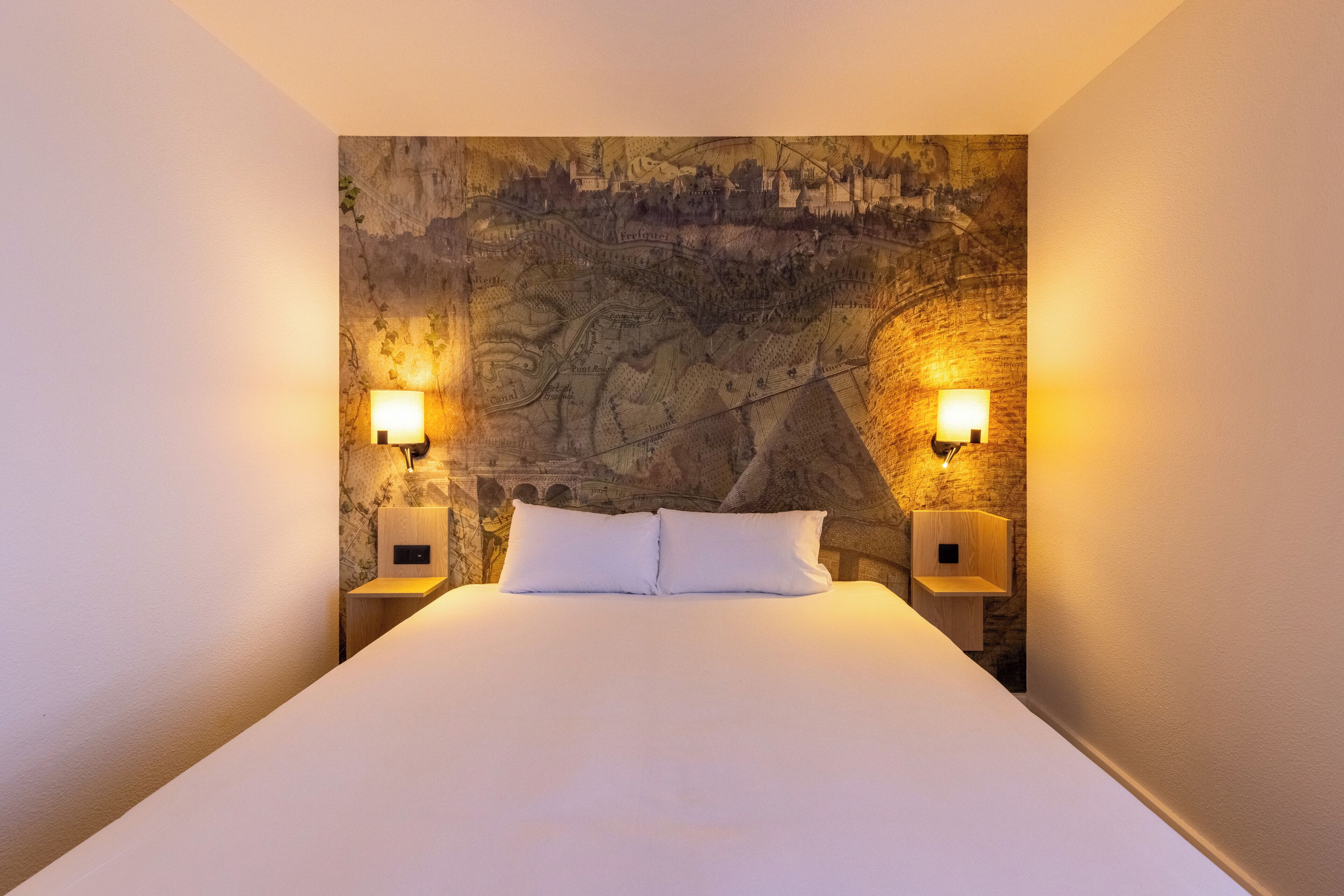 Una cama con sábanas blancas, dos lámparas de noche y una pared con textura.