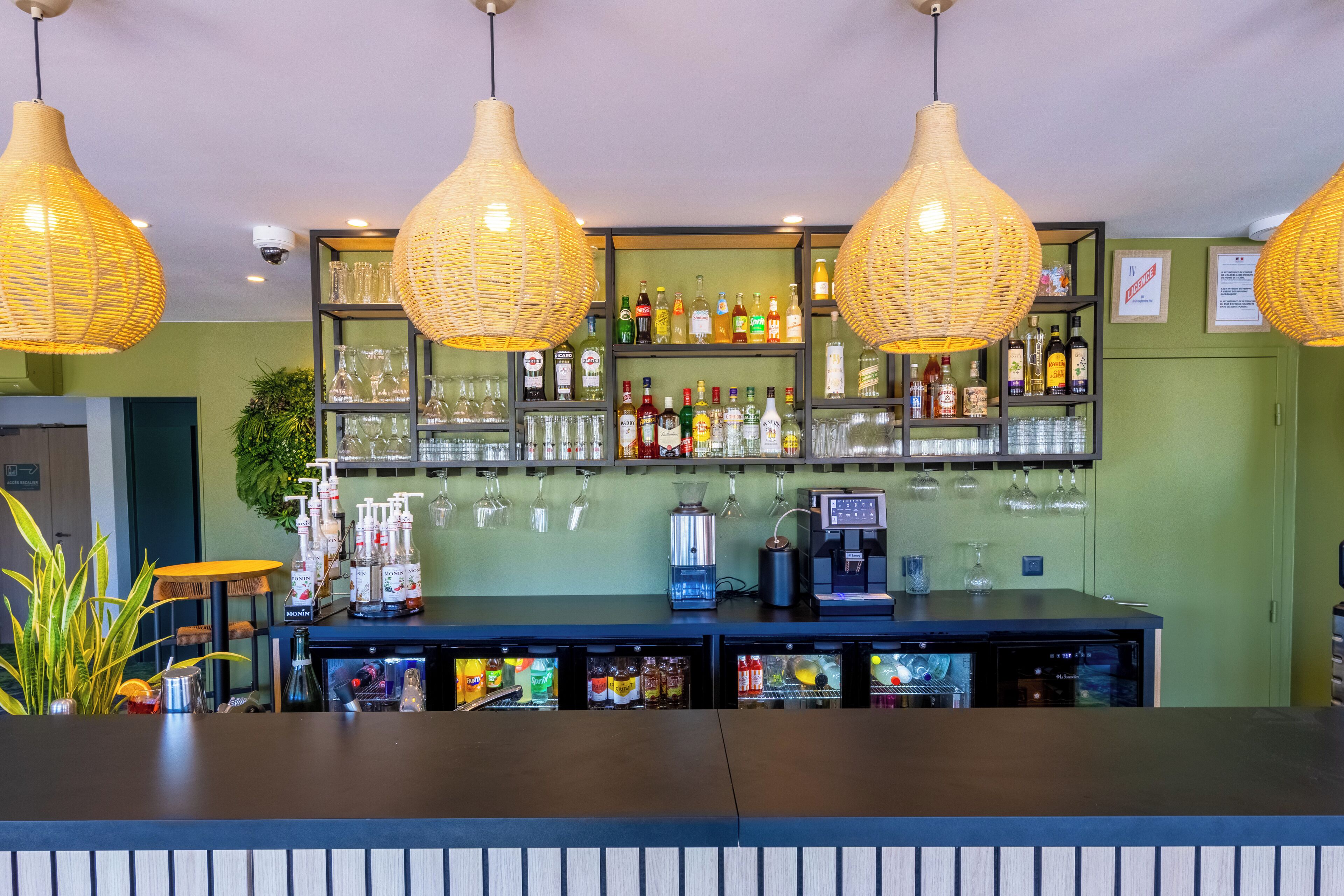 A bar area with wicker pendant lights, shelves of liquor bottles, a coffee machine, and a refrigerated display.
