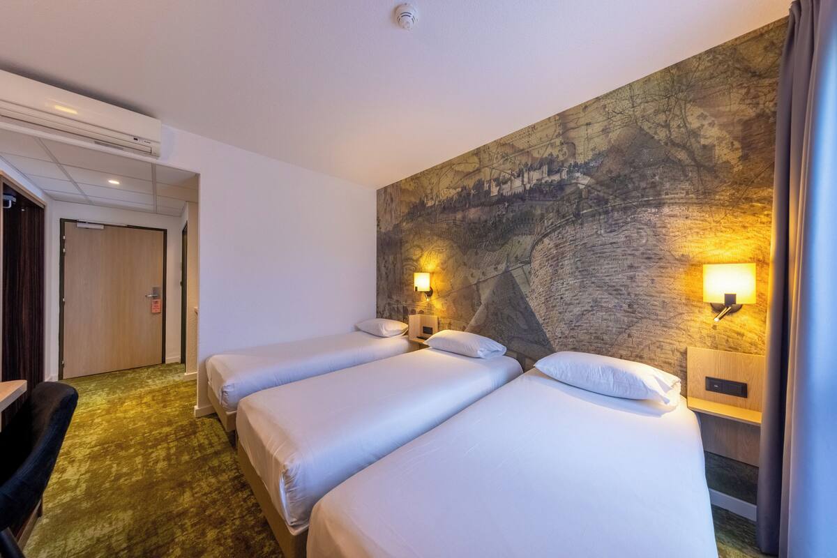 Une chambre d’hôtel avec trois lits simples, un bureau, une chaise et une grande fresque murale.