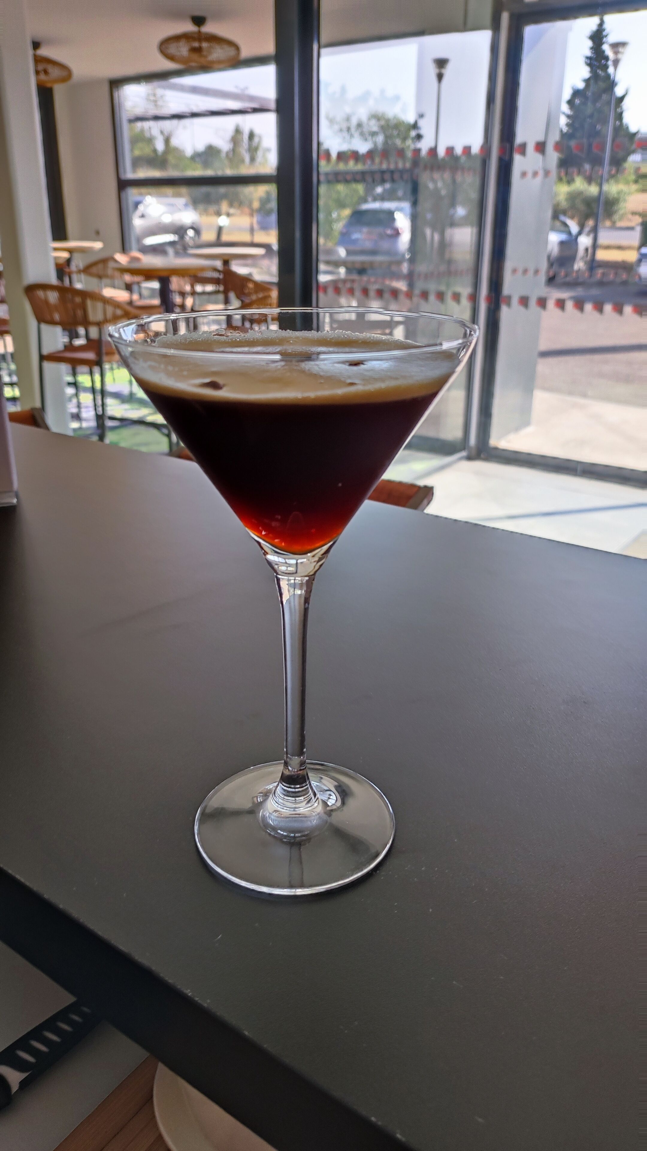 A martini glass with a dark liquid on a table inside a cafe.