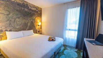 Ein Hotelzimmer mit einem großen Bett, einer Wandmalerei mit einer Karte, einem Schreibtisch mit einem Laptop und einem Fenster mit Vorhängen.