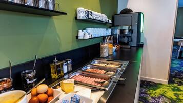 A buffet setup with various food items and beverages, including hot dogs, eggs, and coffee.