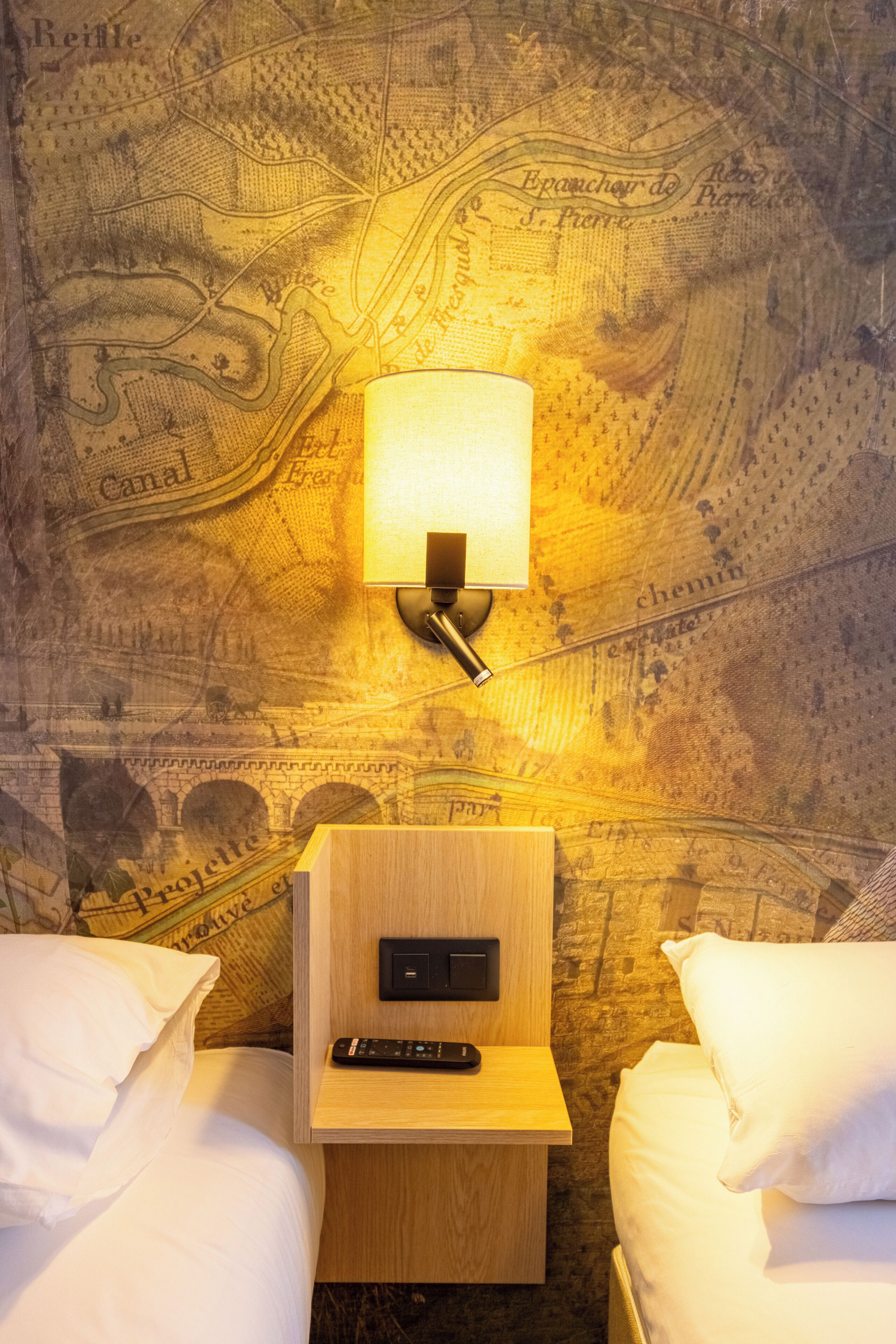 Habitació d'hotel amb un llit, una tauleta de nit amb una làmpada i una paret amb un disseny de mapa.