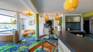 A reception area with a counter, seating, and a large window overlooking a parking area. - Hôtel Pont Rouge, Carcassonne (Carcassonne)