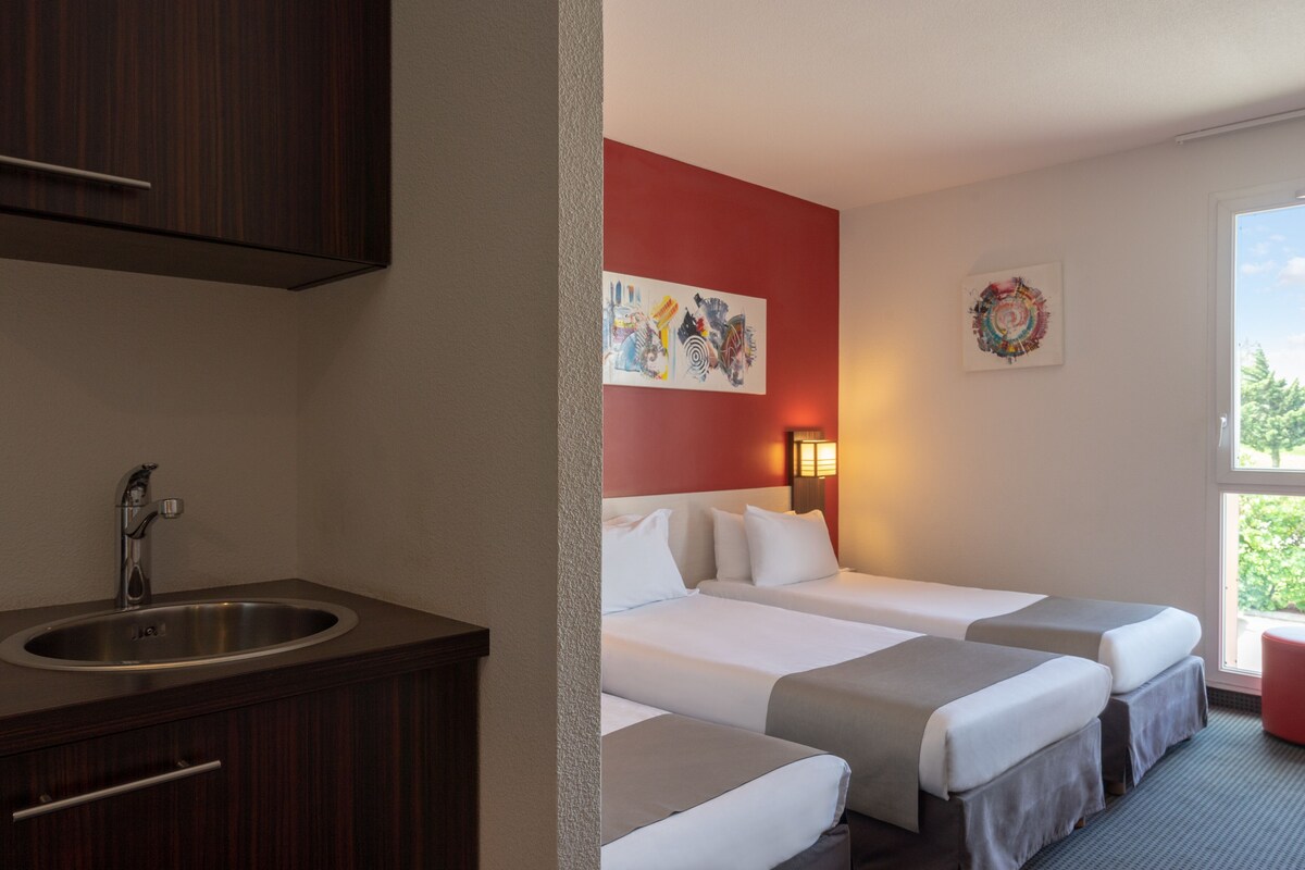 Habitación de hotel con un mueble de madera, un lavamanos, dos camas, una pared de acento roja y obras de arte.