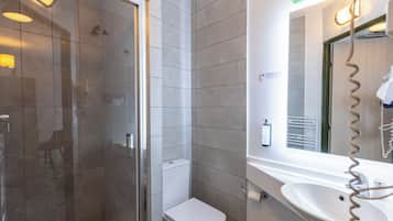 Un bany modern amb una dutxa envidrada amb vidre, un vàter i un lavabo amb mirall.