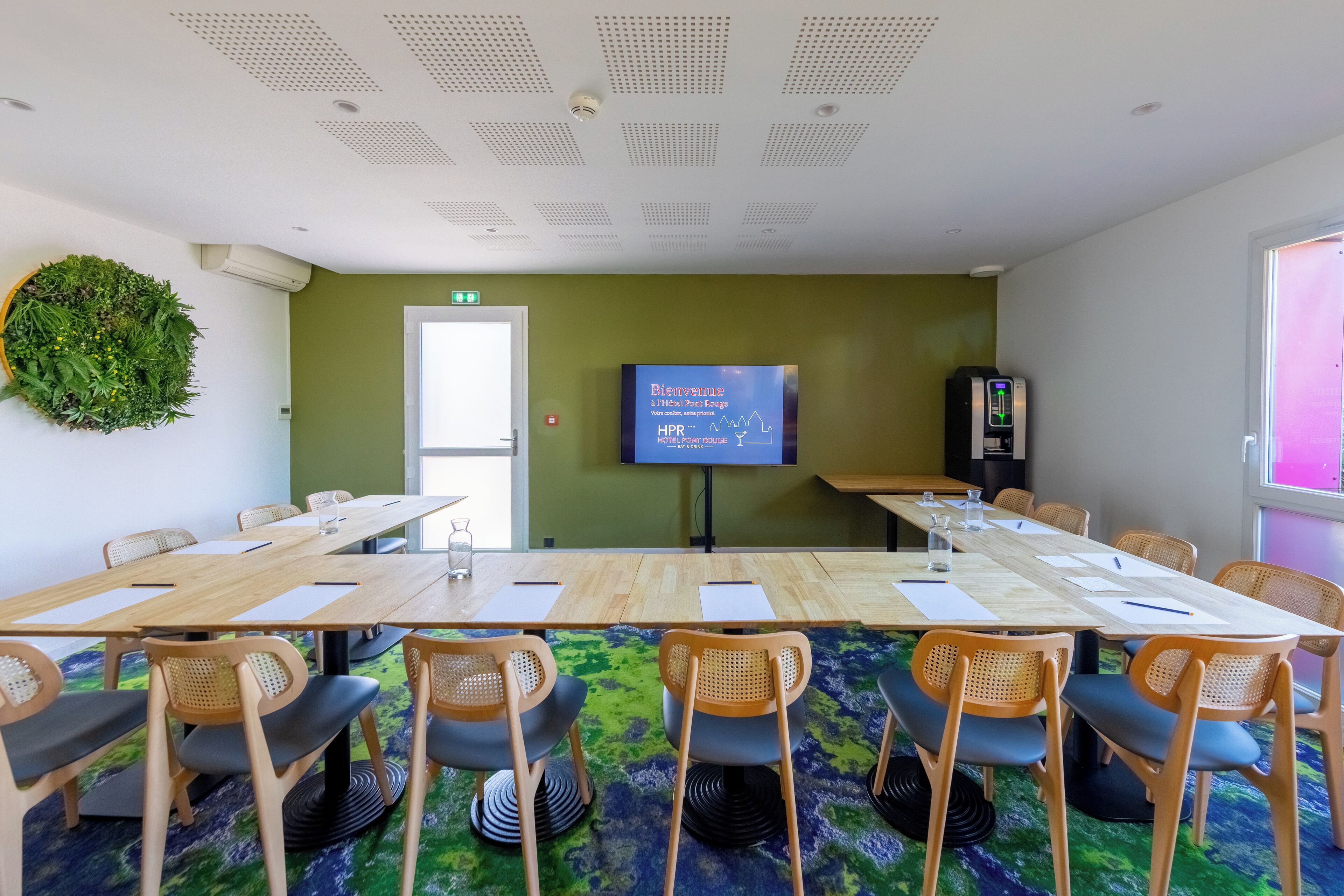 A conference room with a large table, chairs, a projector screen, and a green wall.
