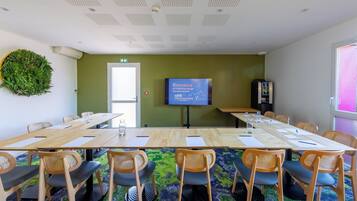 A conference room with a large table, chairs, a projector screen, and a green wall.