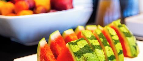 A plate of watermelon slices on a table with a bowl of mixed fruits in the background.