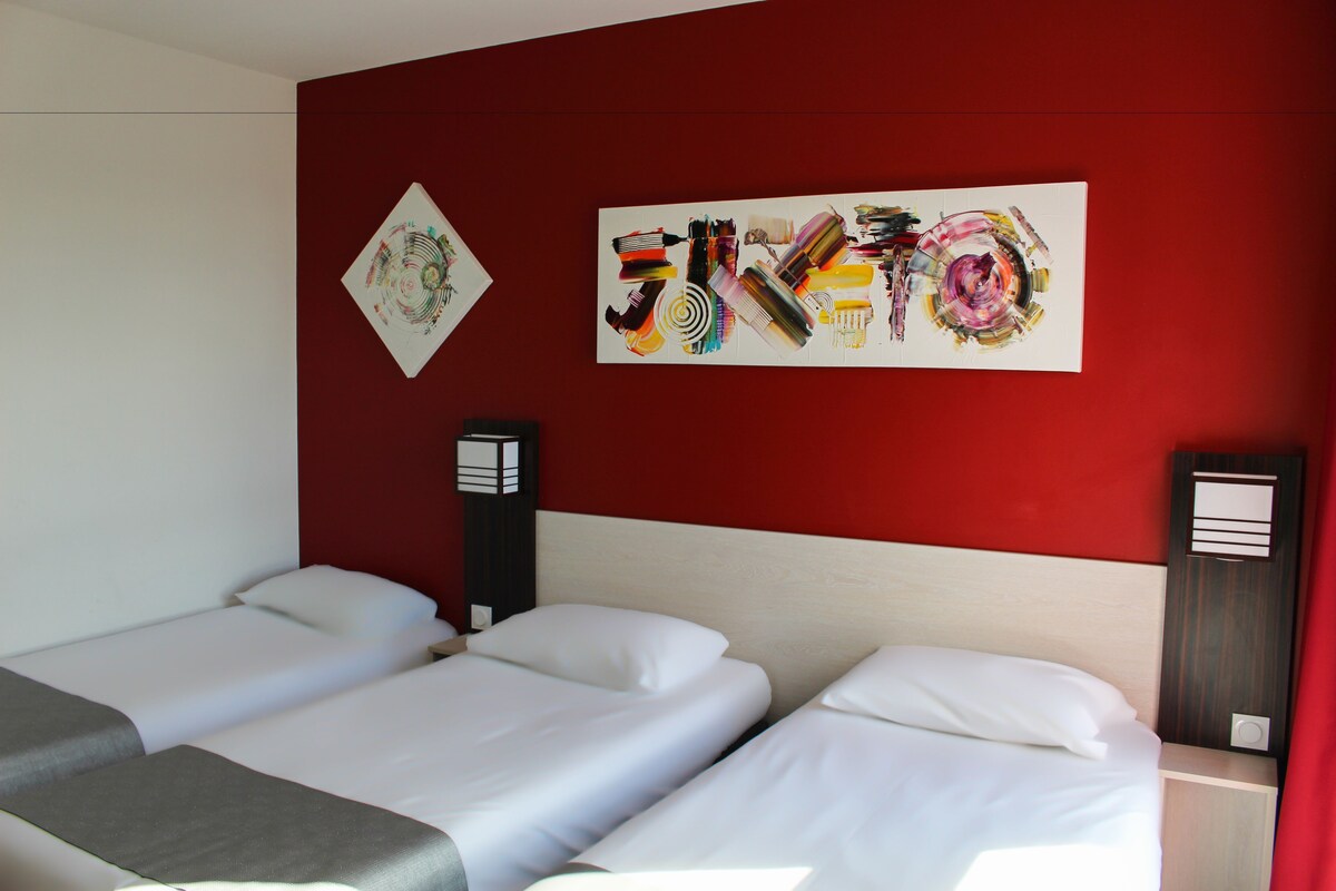 Habitación de hotel con dos camas, una pared roja y obras de arte.