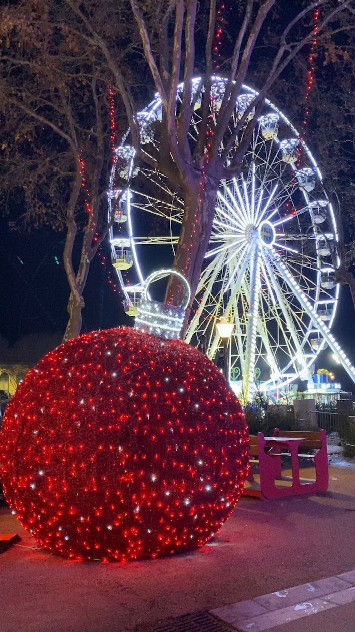 A large illuminated sphere and a Ferris wheel at night.