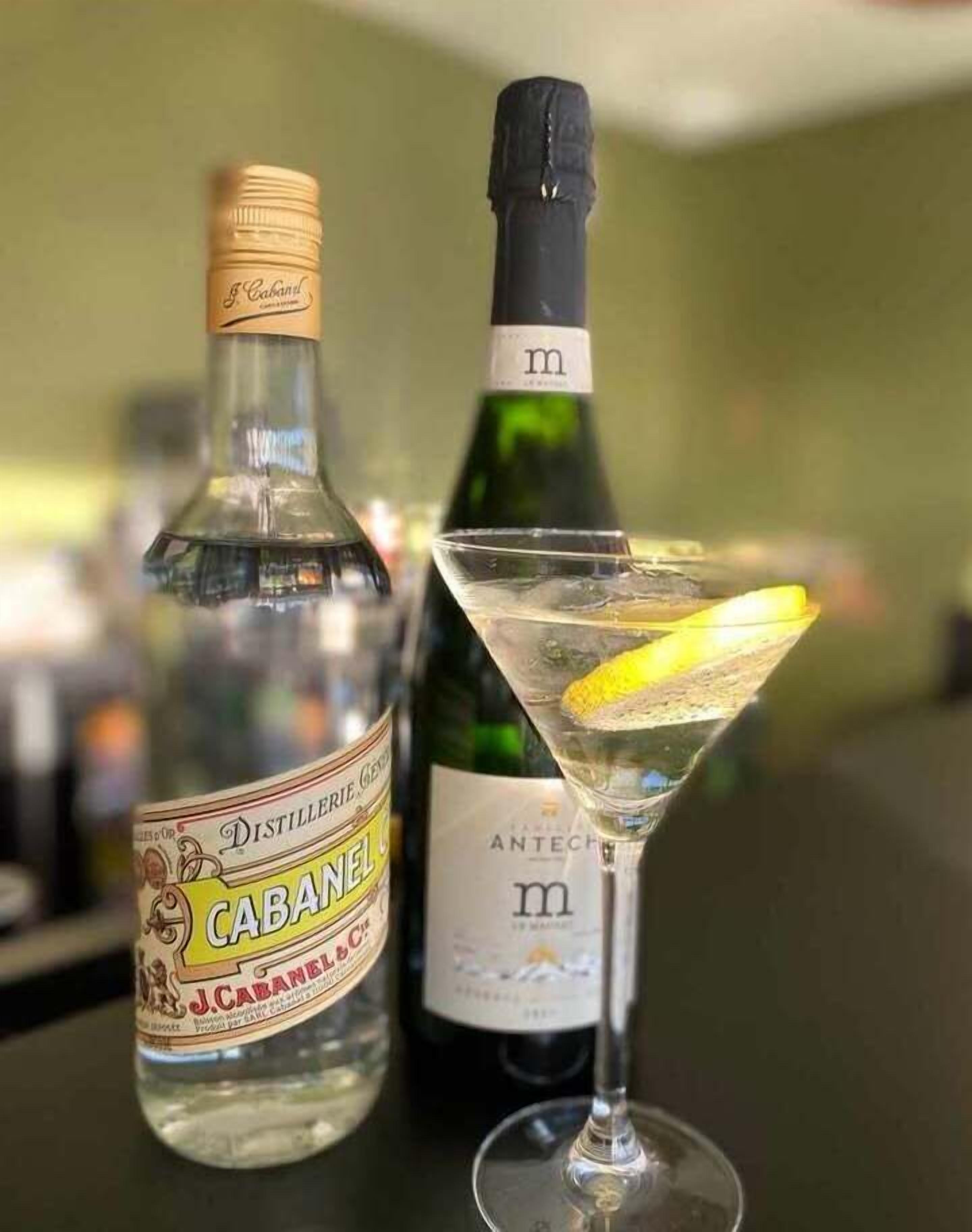 Deux bouteilles de gin J. Cabanel et un verre à martini avec une tranche de citron sur le comptoir d’un bar.