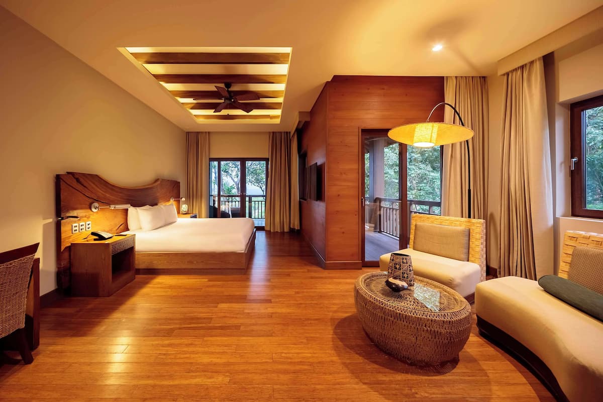 A spacious hotel room with a large bed, a sofa, a small round table, and a ceiling fan.