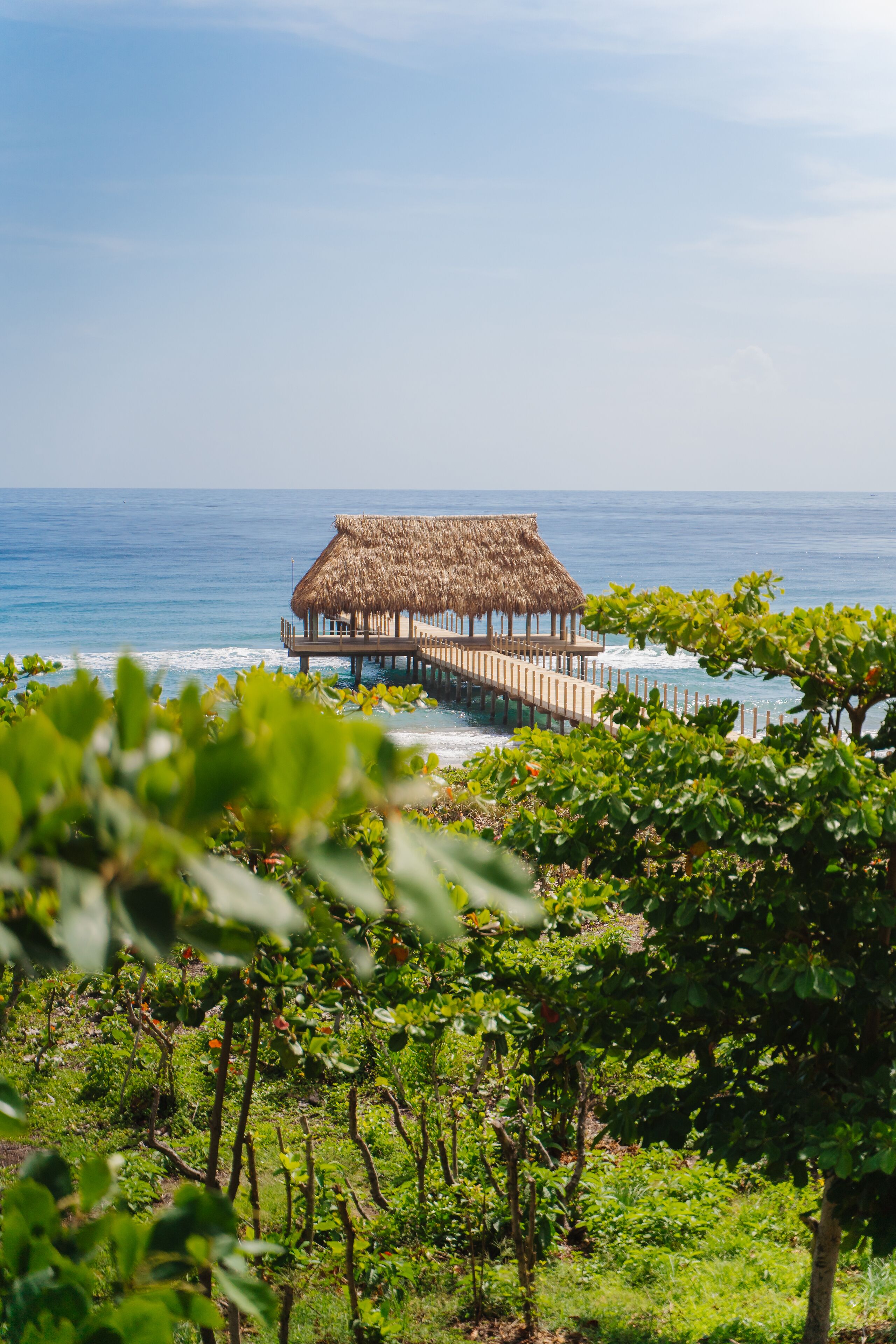 A thatched-roof structure extending over the water, connected to land by a pier.