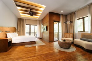 A modern hotel room with a wooden ceiling, a bed, a sofa, a round wicker coffee table, and a large window with curtains.