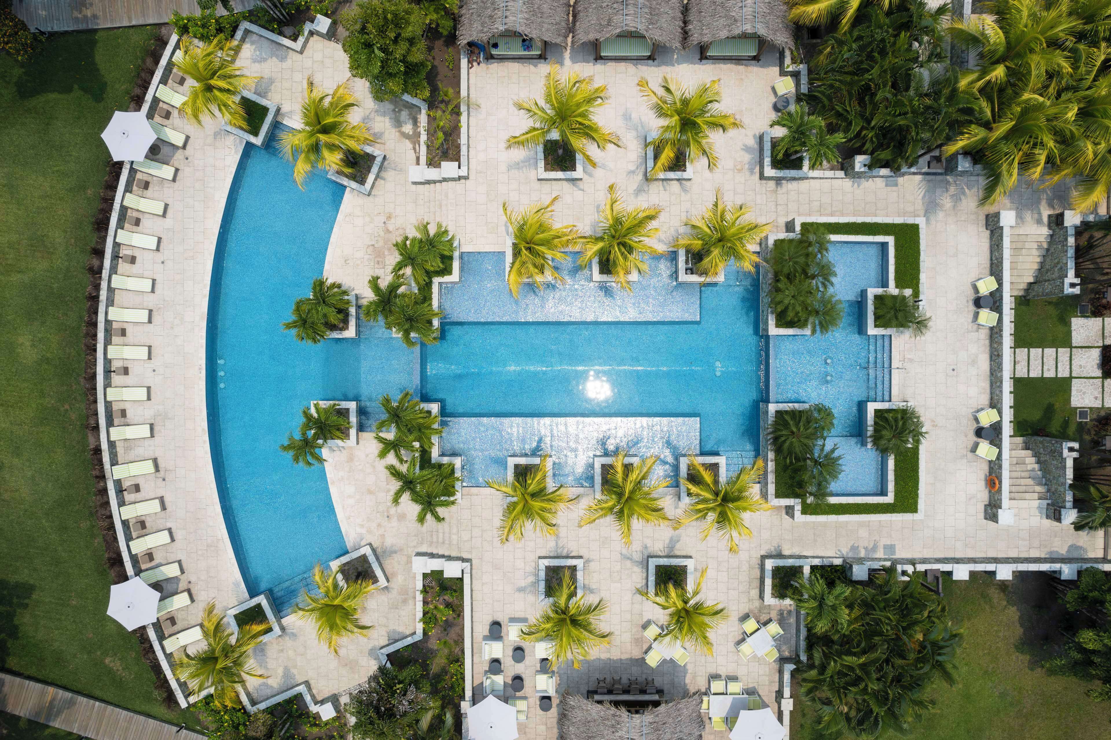 Vista aérea de un resort con una piscina central rodeada de áreas de descanso y palmeras.