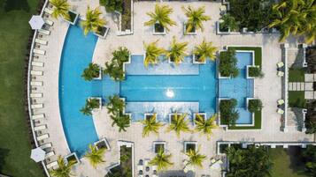 Vista aérea de un resort con una piscina central rodeada de áreas de descanso y palmeras.