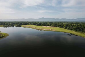 A serene landscape with a calm lake, lush greenery, and distant mountains under a clear sky.