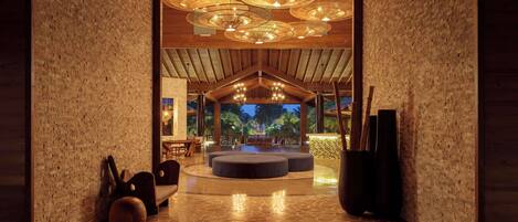 A spacious lobby with a high ceiling, brick walls, and a central seating area with ottomans.