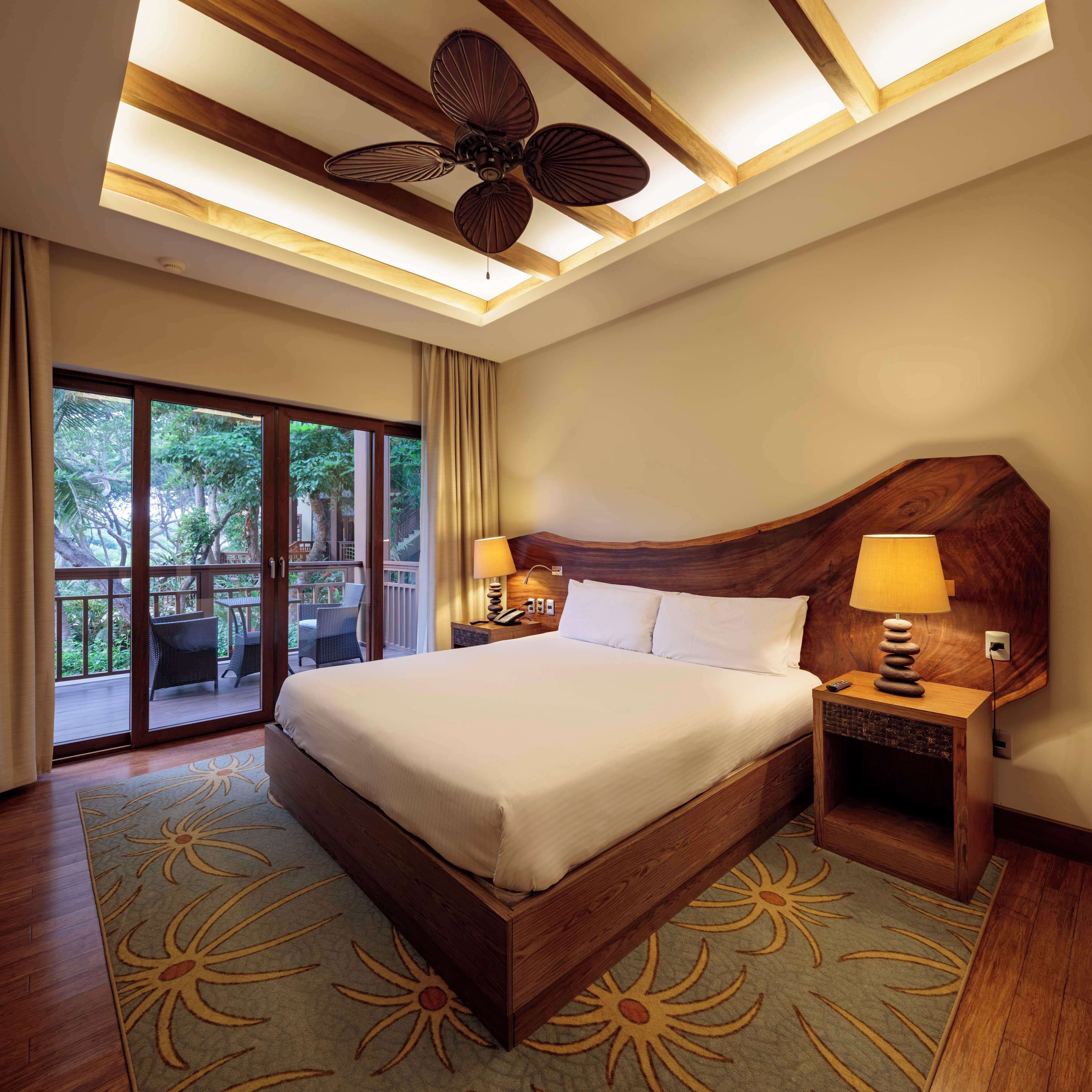 A spacious bedroom with a large bed, a ceiling fan, and a view of the outdoors through a sliding glass door.