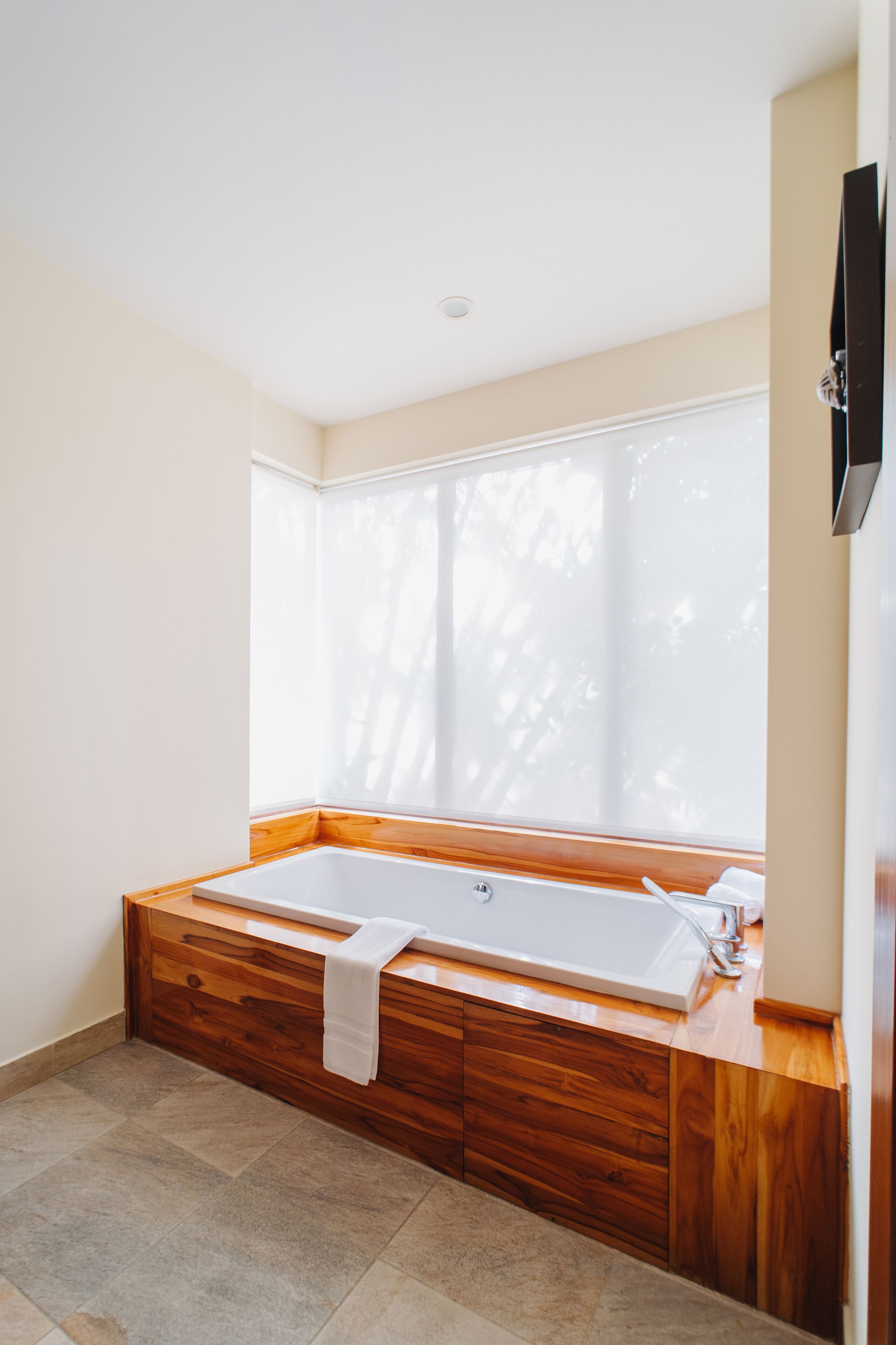 Een moderne badkamer met een groot bad, houten kasten en een raam met jaloezieën.