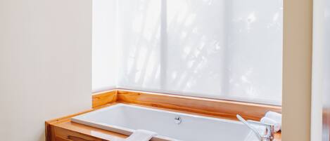 Een moderne badkamer met een groot bad, houten kasten en een raam met jaloezieën.