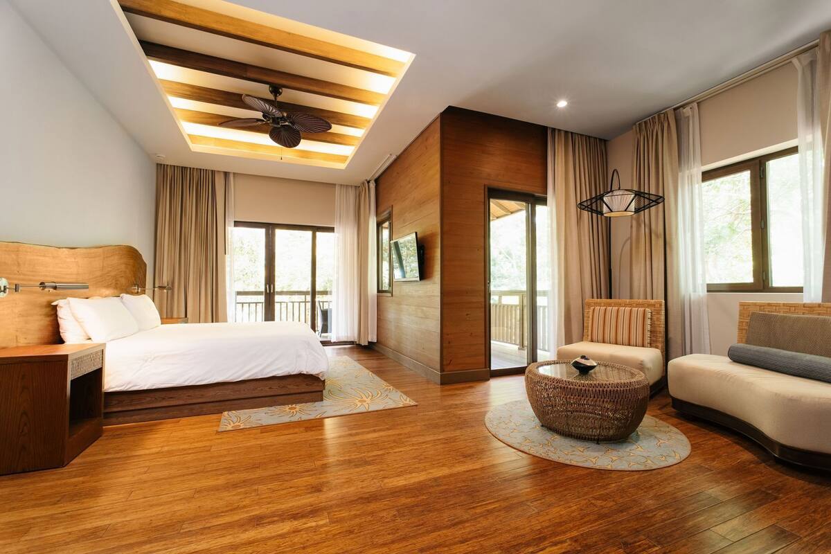 A modern hotel room with a wooden floor, a bed, a sofa, a coffee table, and a balcony.