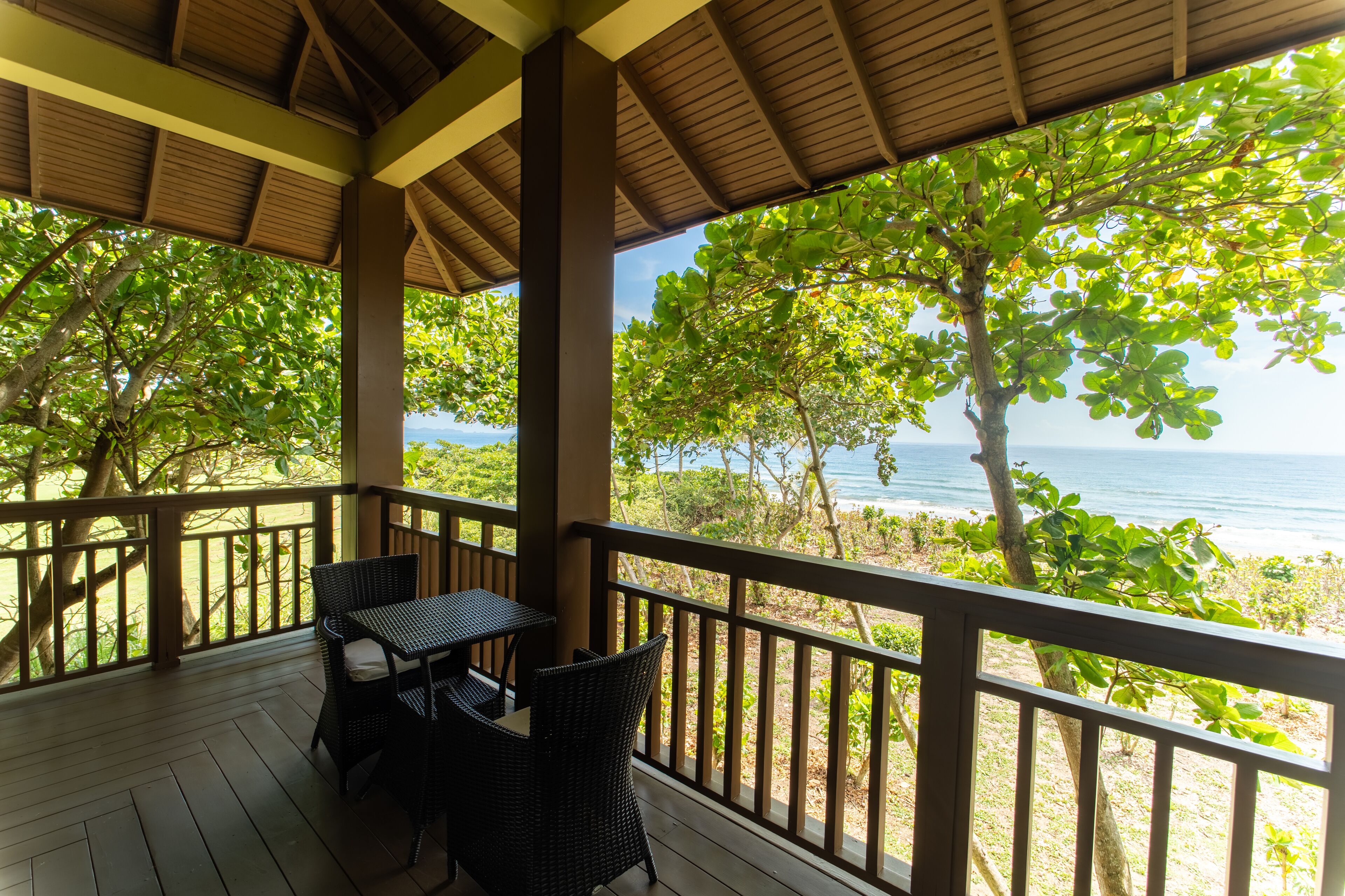 A covered outdoor area with a table and chairs, overlooking a beach and ocean.