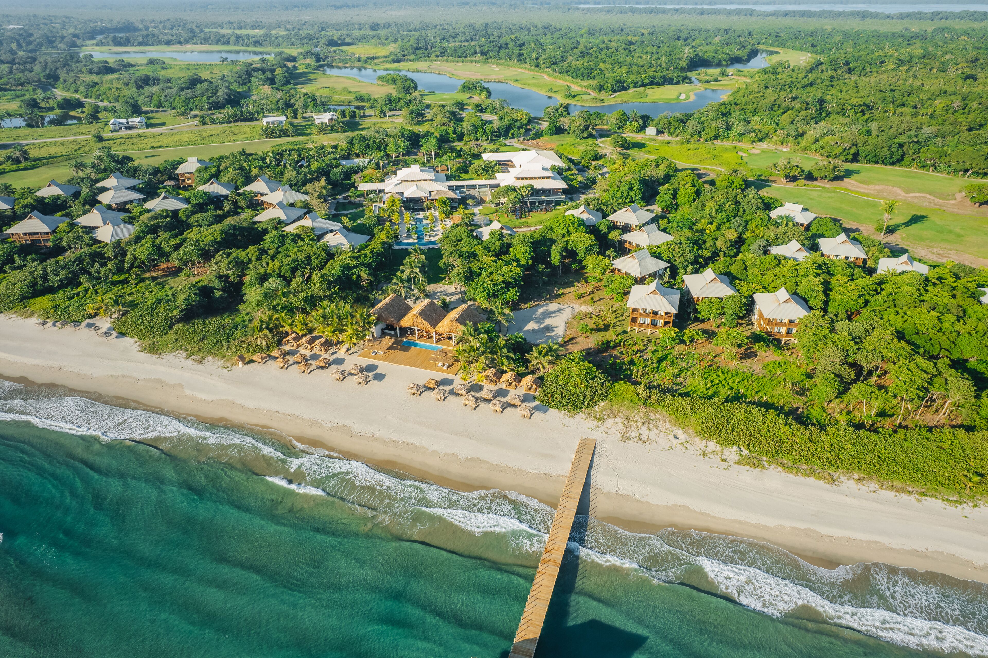 An aerial view of a resort with beachfront properties, a golf course, and a water body.