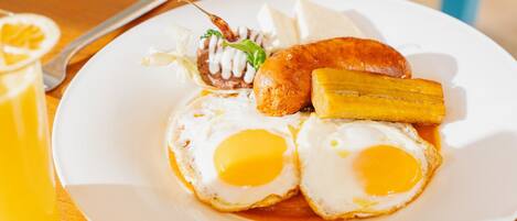 Un plato de desayuno con huevos, una salchicha y una rodaja de plátano sobre un plato blanco.