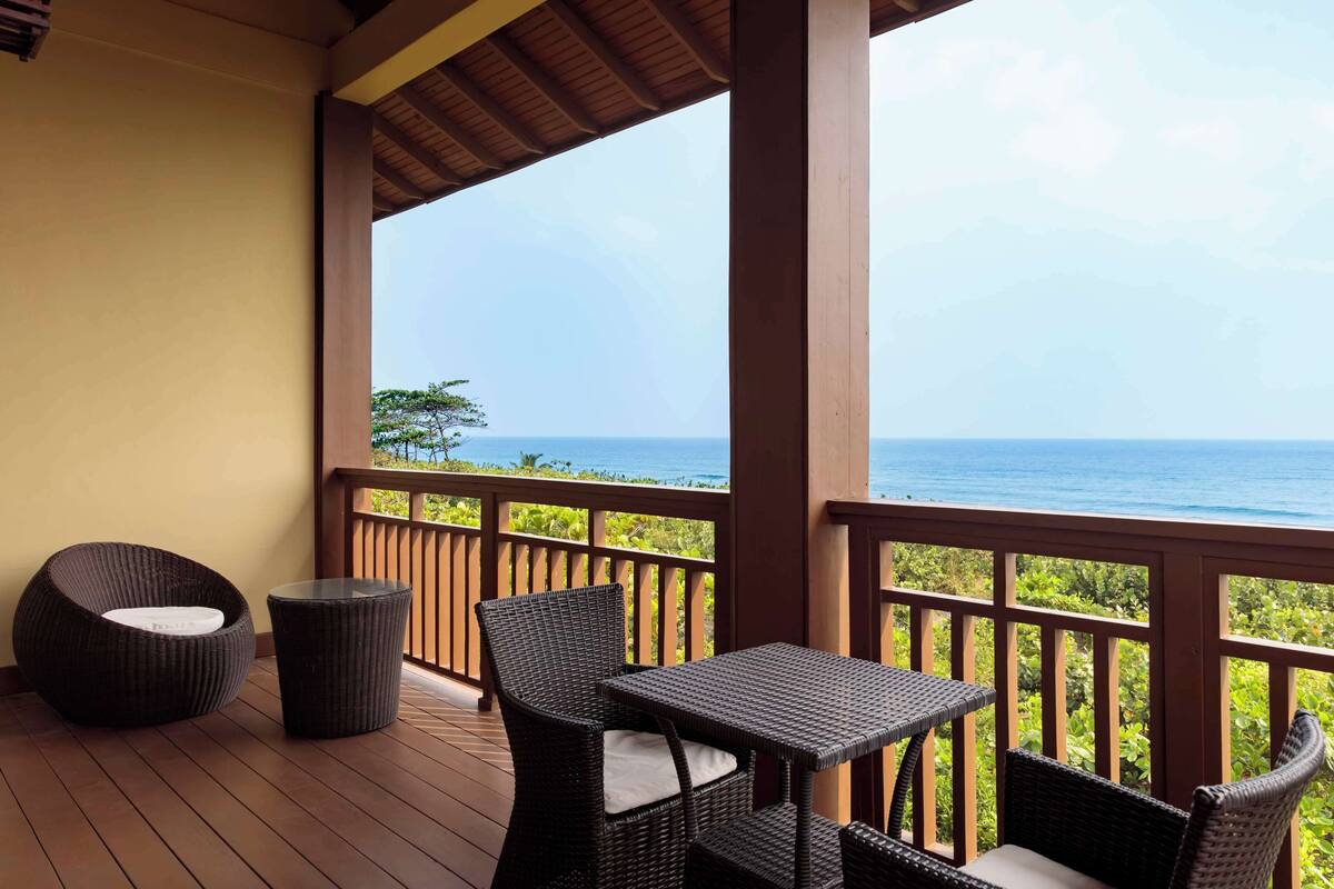 A covered outdoor seating area with wicker furniture and a view of the ocean.