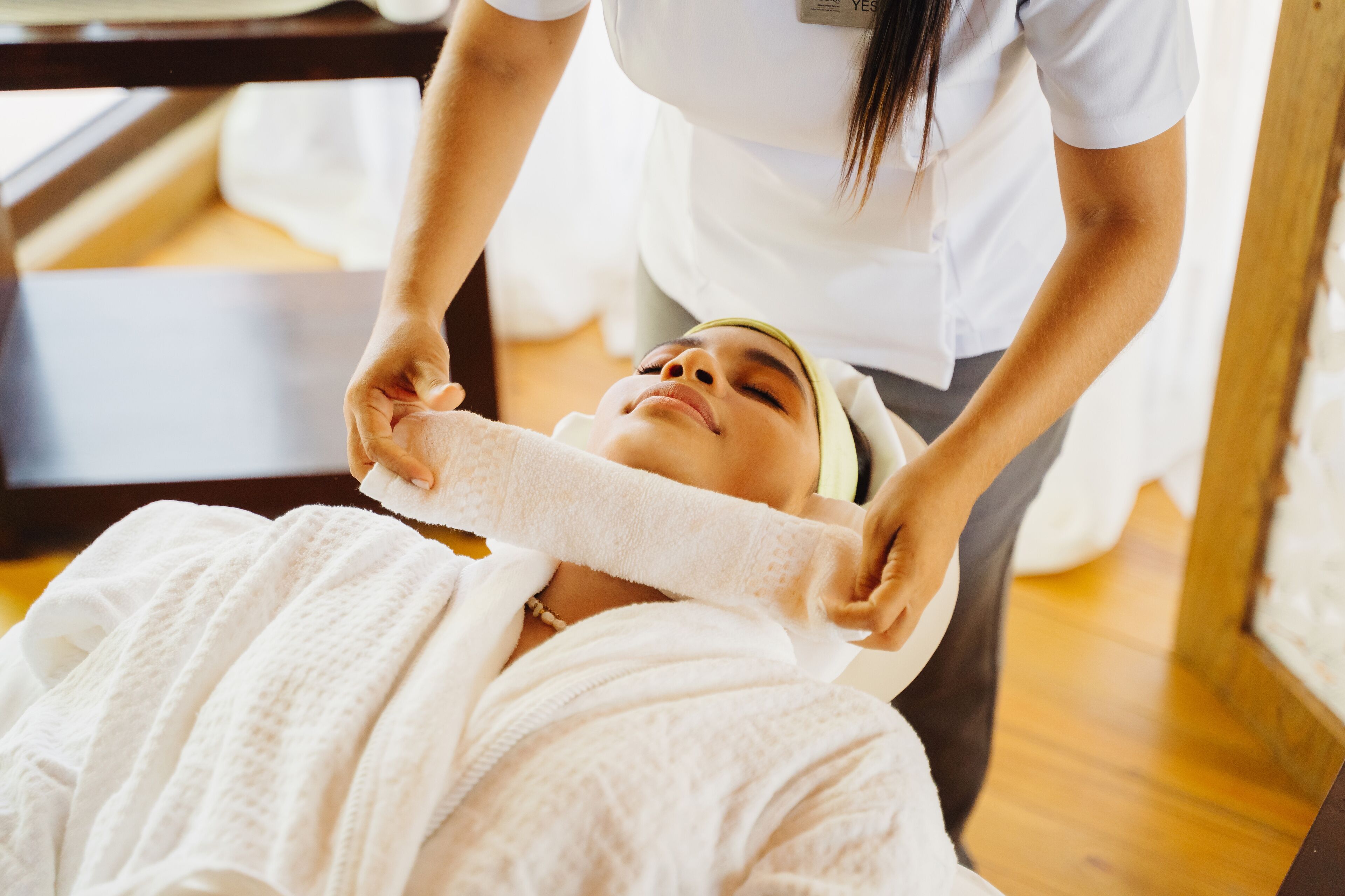 A person receiving a shoulder treatment in a room with wooden flooring and a window in the background.