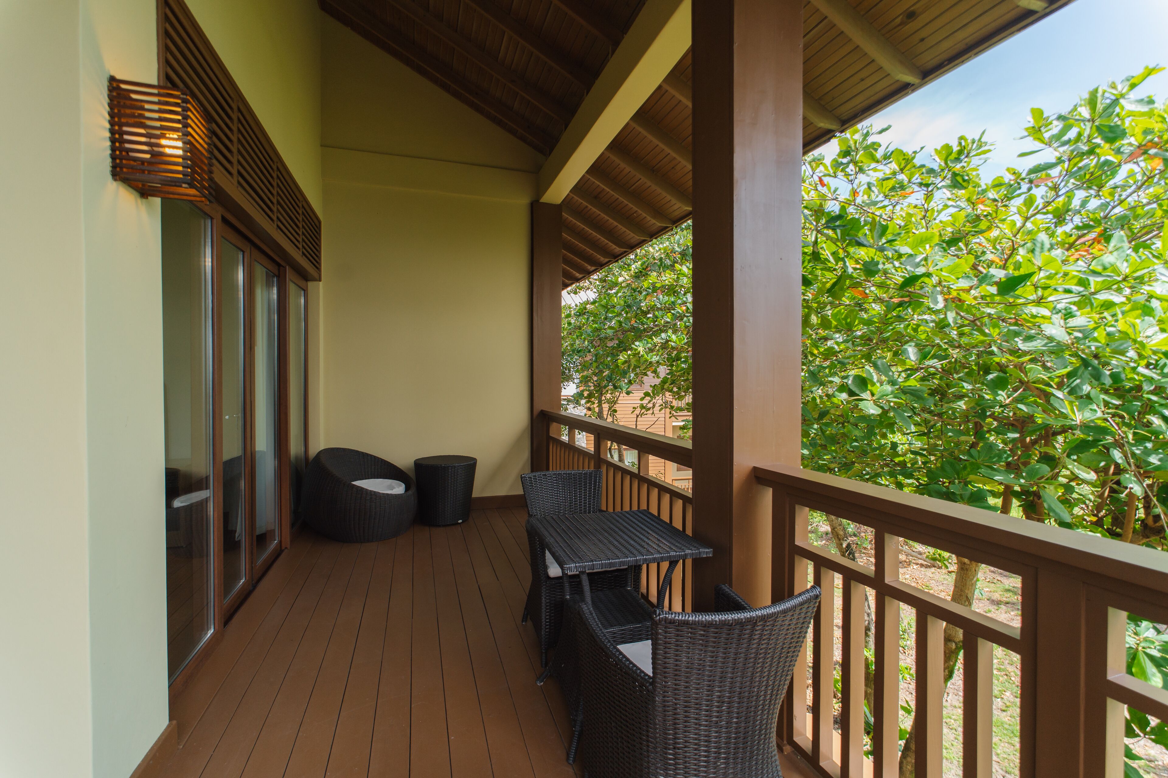 A balcony with wicker furniture, a trash bin, and a view of greenery.