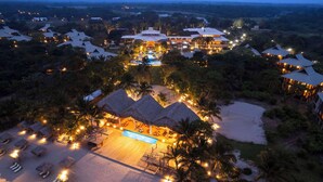 A resort with multiple thatched-roof buildings, a central pool, and a beach area with sun loungers. - Indura Beach & Golf Resort, Curio Collection by Hilton (Tela)