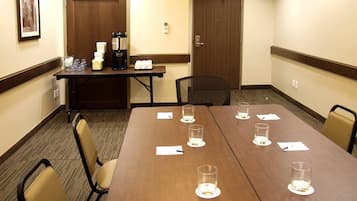 Un salón de conferencias con una mesa larga, sillas, una estación de café y una puerta de salida.