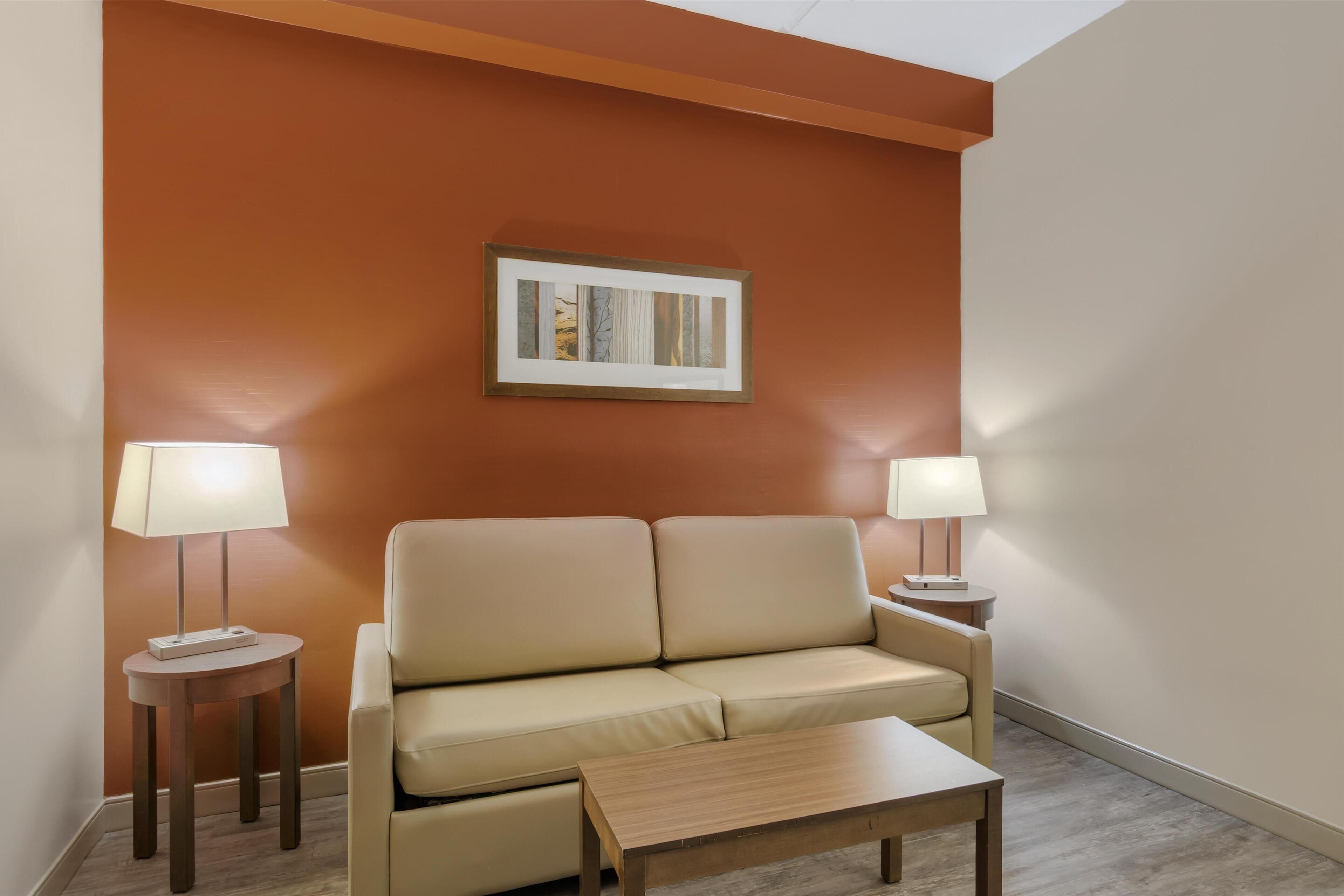 Una habitación con un sofá color beige, dos mesitas de noche con lámparas, un cuadro en la pared y una mesa de centro de madera.