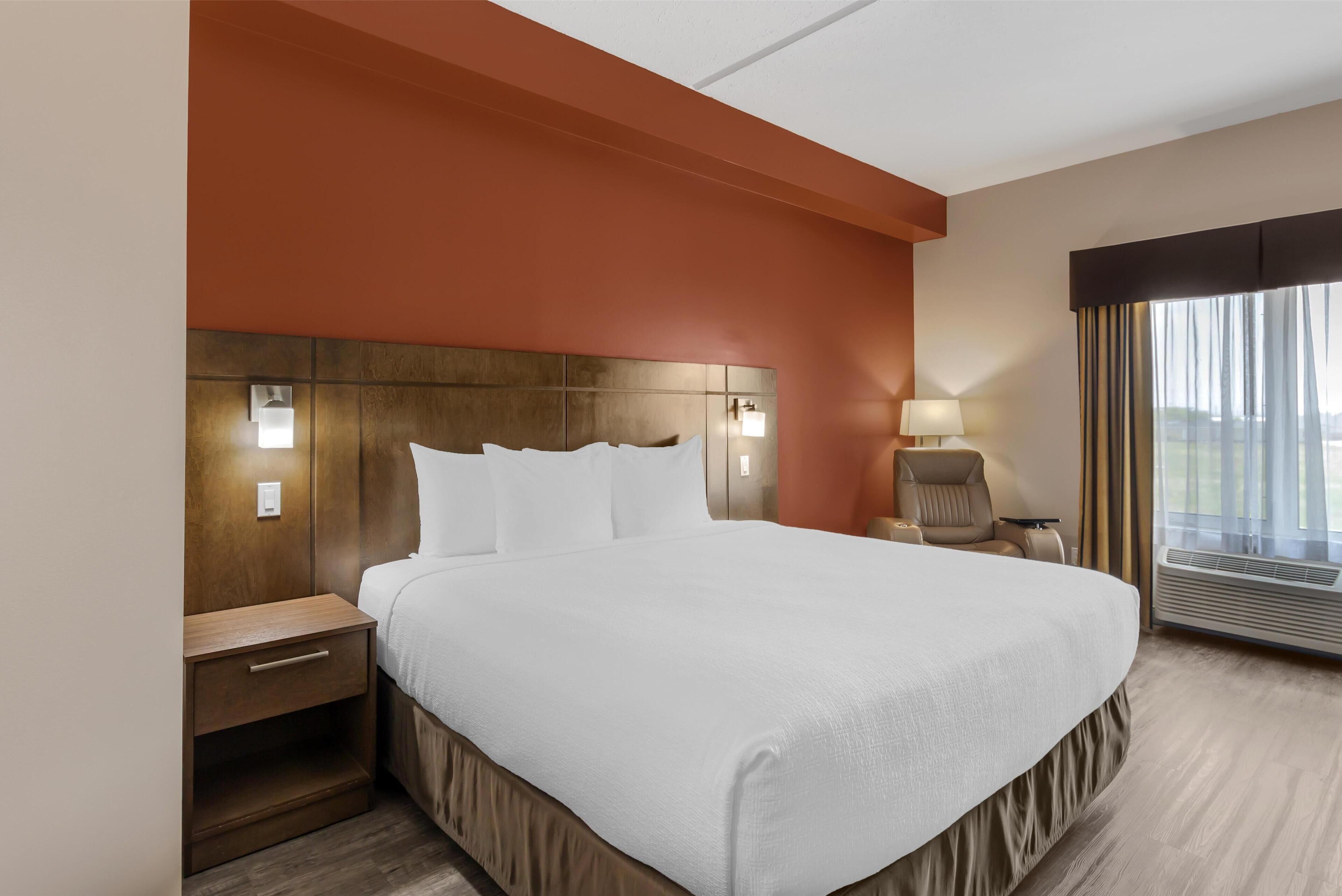 A hotel room with a large bed, a nightstand, a lamp, and a window with curtains.