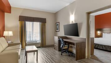 Una habitación de hotel con cama, escritorio con silla, televisión, sofá y ventana con cortinas.