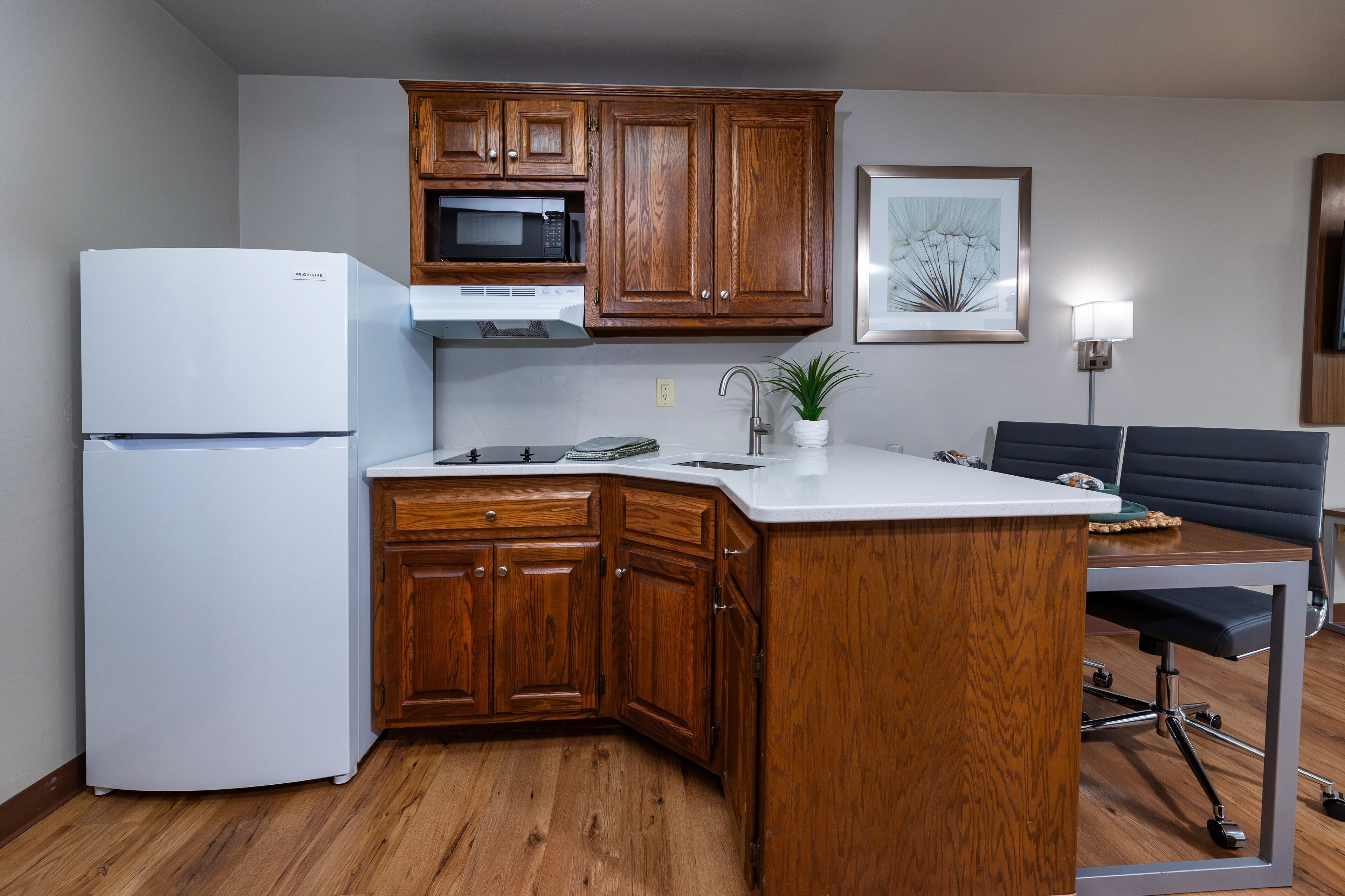 A compact kitchen with wooden cabinets, a white refrigerator, a microwave, and a sink.