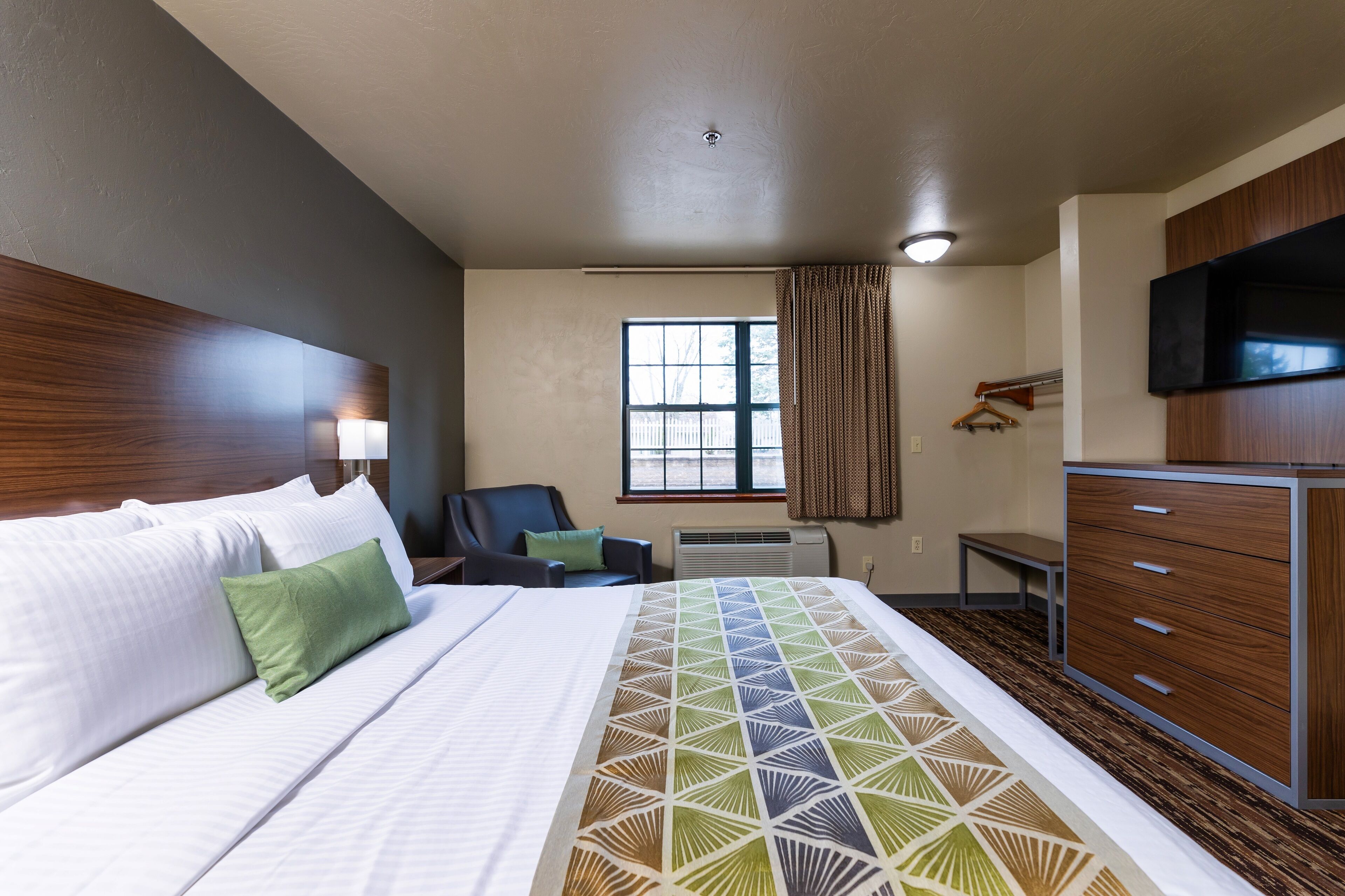 A hotel room with a large bed, a chair, a desk, a television, and a wardrobe.