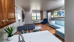 A modern living room with a sofa, a chair, a dining table, and a kitchen area with a sink and a potted plant. - Extended Stay Airport (Green Bay)