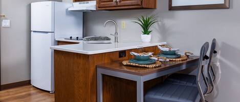 Une cuisine compacte avec des meubles en bois, un réfrigérateur blanc, un four à micro-ondes et un petit îlot central doté d’un évier.