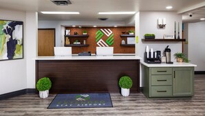 A reception area with a wooden reception desk, a coffee station, and a wall-mounted plant. - Extended Stay Airport (Green Bay)